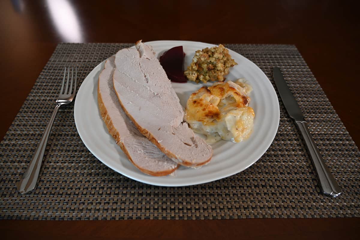 Side view image of a white plate with turkey, stuffing, scalloped potatoes and cranberry sauce served on it.