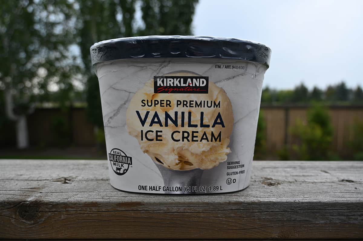 Image of one 1.89 liter tub of ice cream sitting on a deck with trees in the background.