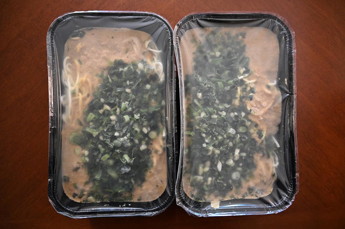 Top down image of two unopened trays of Dan Dan Noodles sitting on a table.