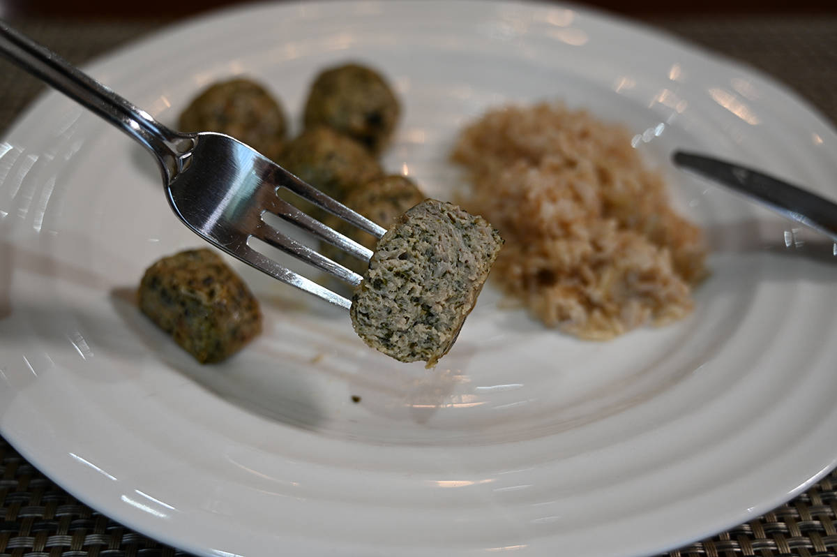 Image of a fork with half a meatball on it so you can see the center of the meatball, in the background is a plate with more meatballs and rice on it.