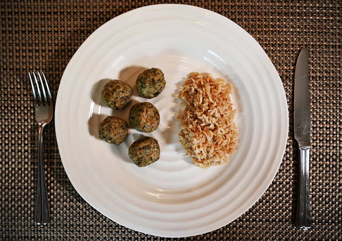 Top down image of five cooked meatballs served on a white plate beside a bed of rice.