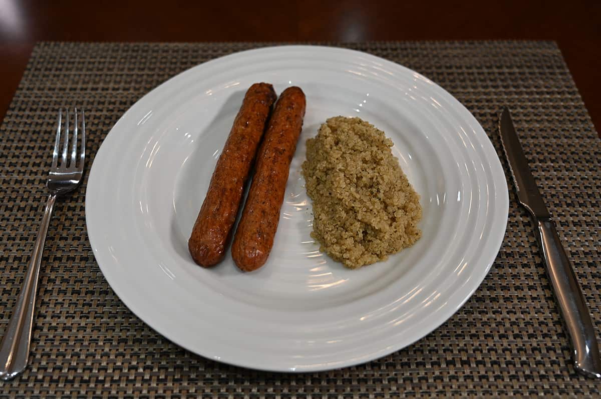 Top down image of two cooked andouille sausages served beside a side of quinoa on a white plate.