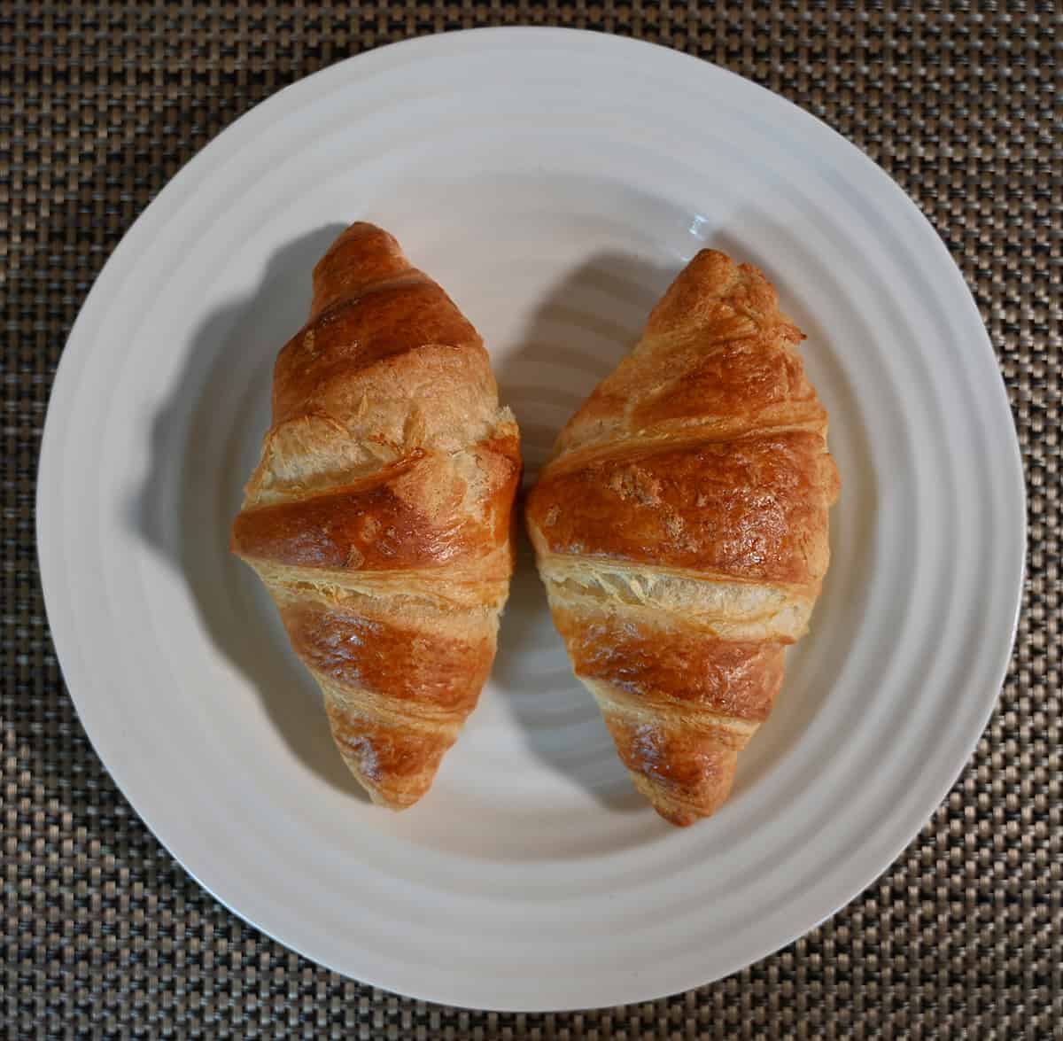 Top down image of two baked croissants served on a white plate.