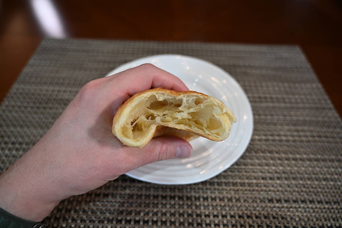 Closeup image of a hand holding a croissant with a few bites taken out of it close to the camera so you can see the center.