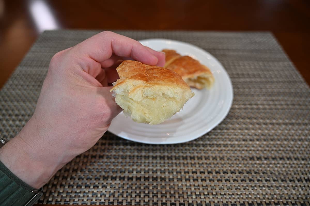 Closeup image of a hand holding a piece of croissant that's been torn off so you can see how flaky the croissant is.