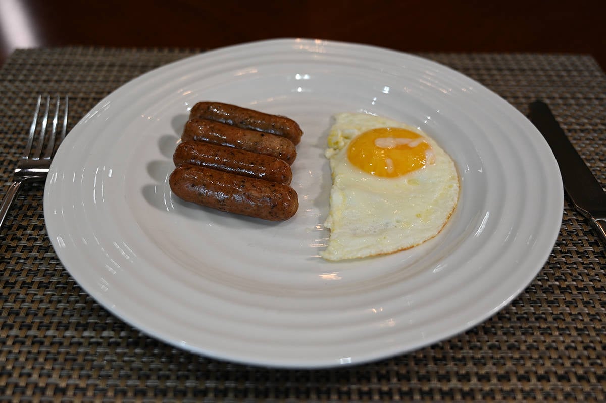 Side view image of four breakfast links served on a white plate beside a sunny side up egg.