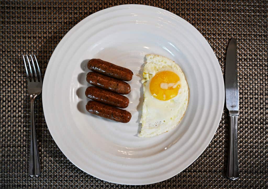 Top down image of four breakfast links served on a white plate beside a sunny side up egg.