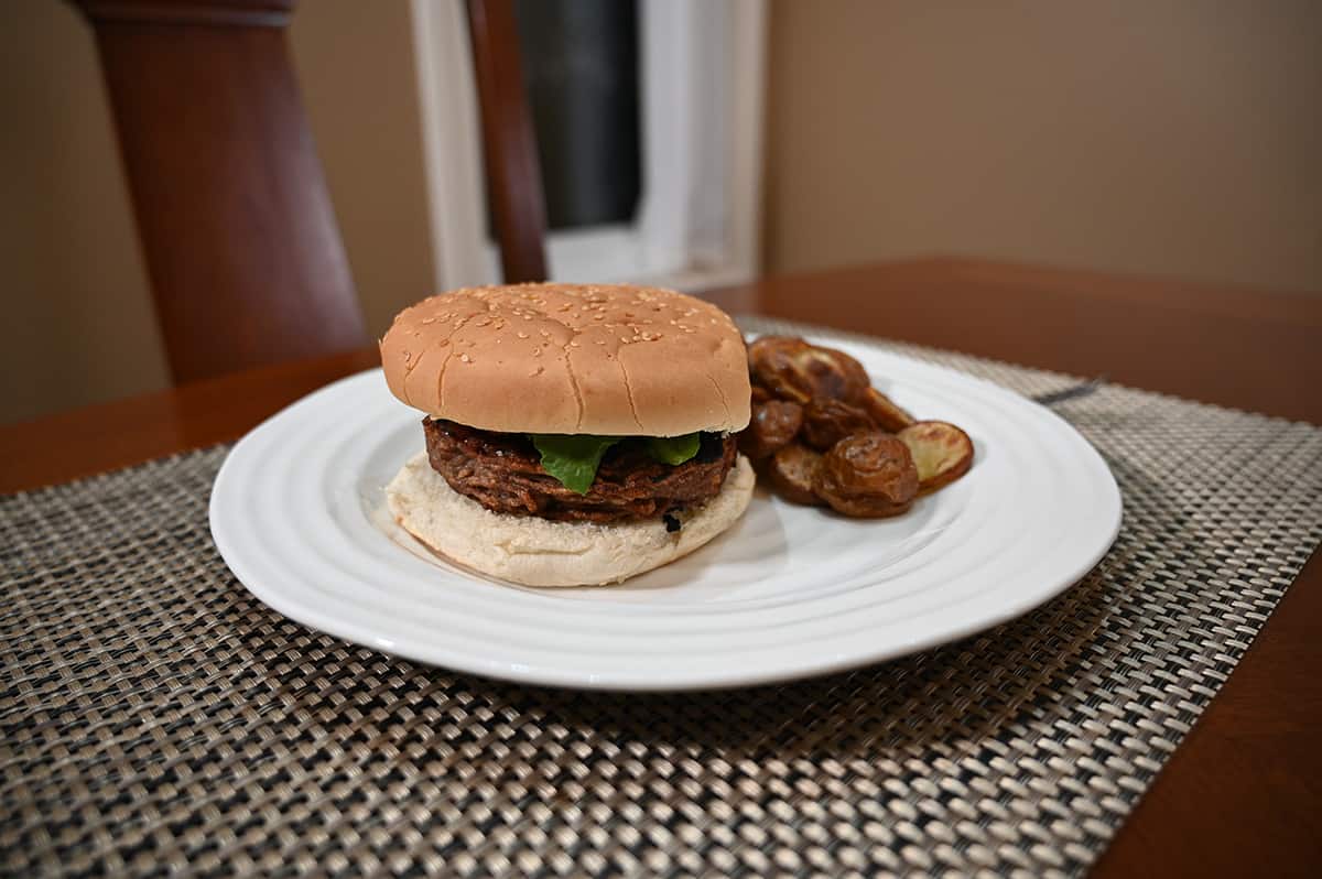 Side view image of a hamburger beside potatoes served on a white plate.