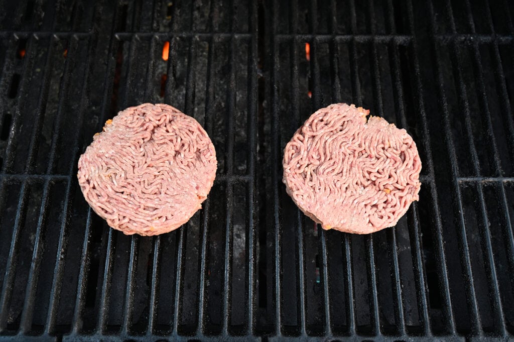 Top down image of two raw burger patties being cooked on a barbecue.