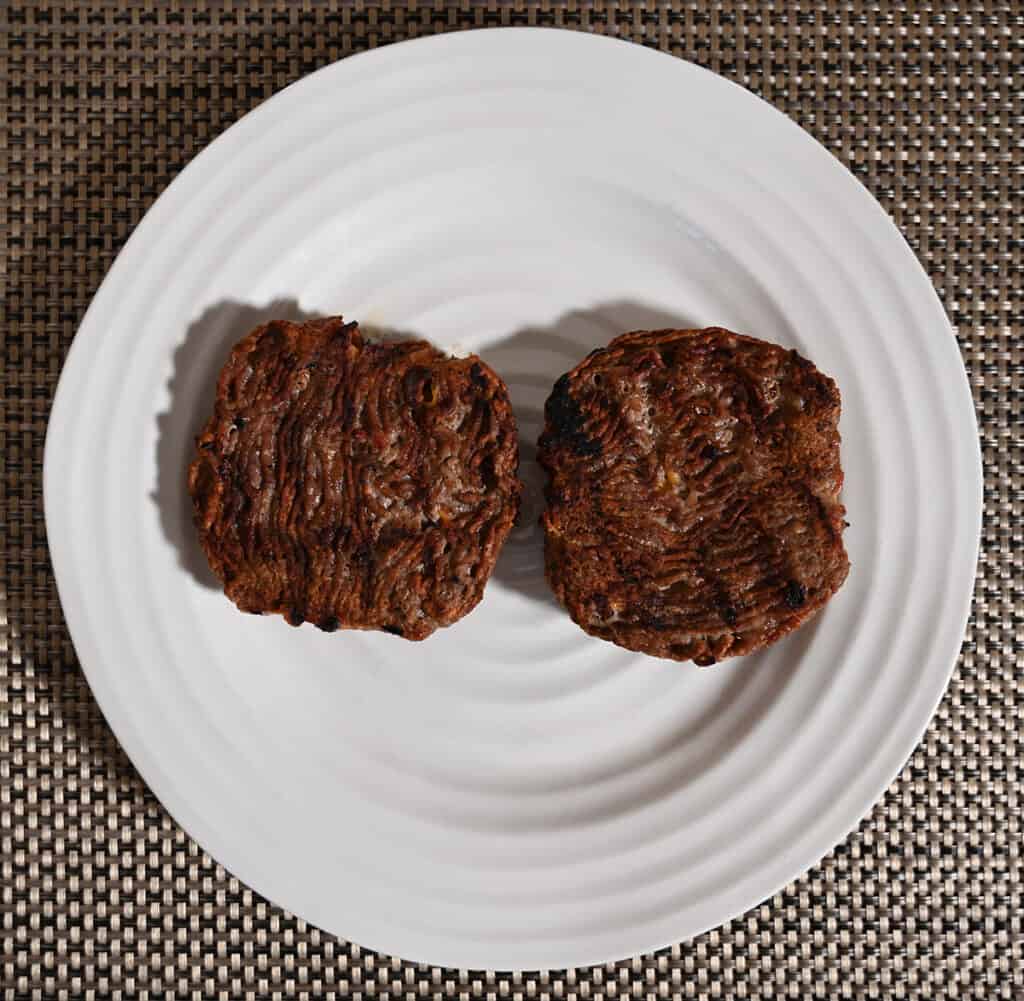 Top down image of two cooked burger patties on a white plate.
