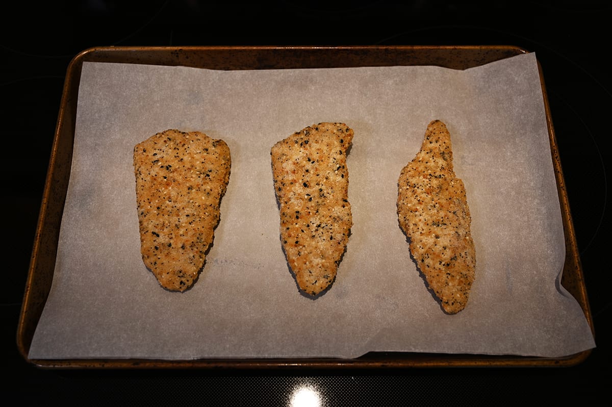 Top down image of three pieces of baked cod laying on a cookie tray lined with parchment paper after being baked.