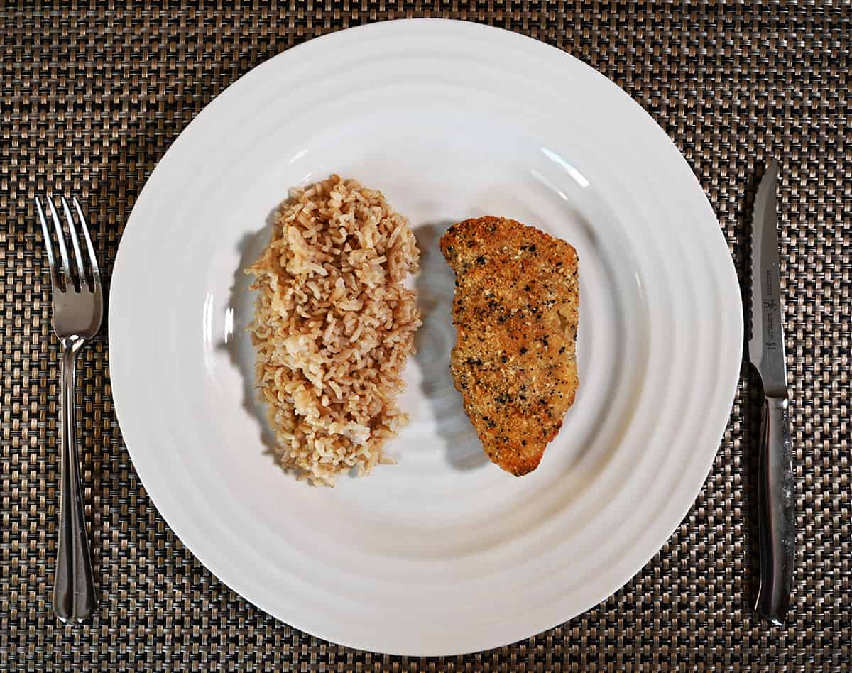 Top down image of a piece of baked cod beside a bed of rice served on a white plate.