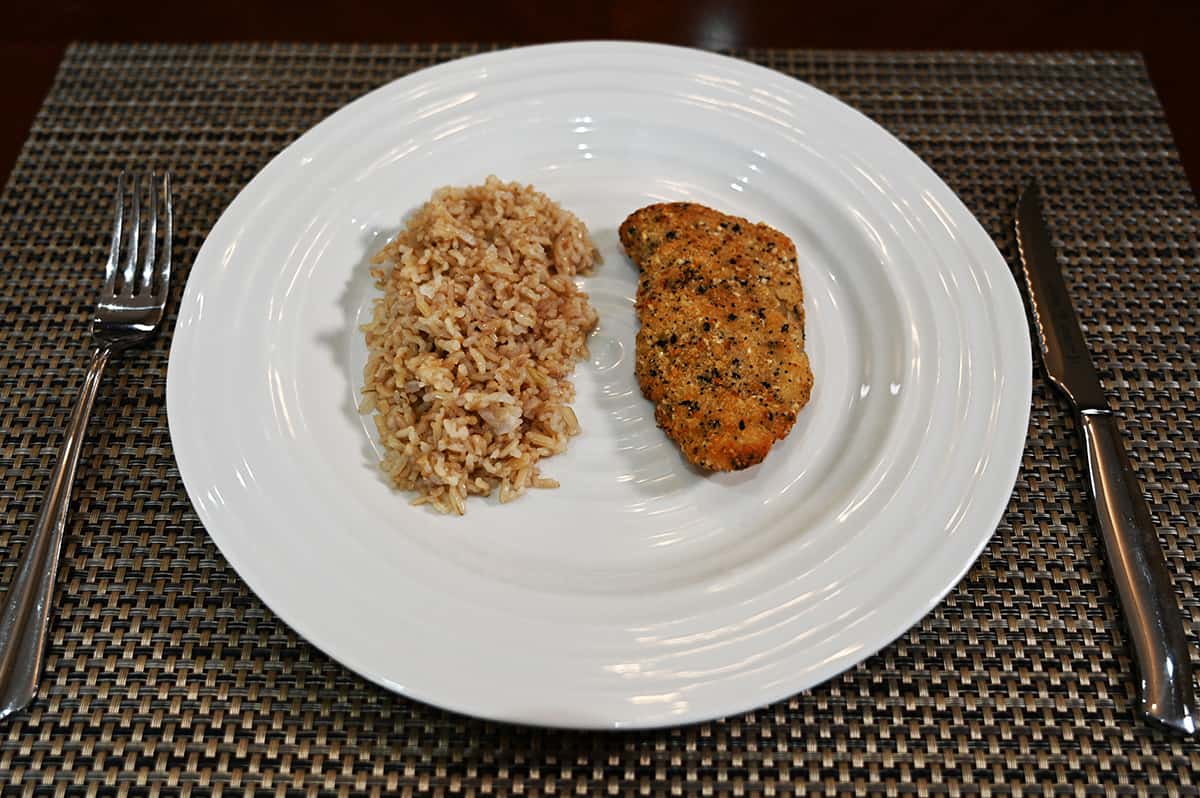 Side view image of a piece of baked cod beside a bed of rice served on a white plate.