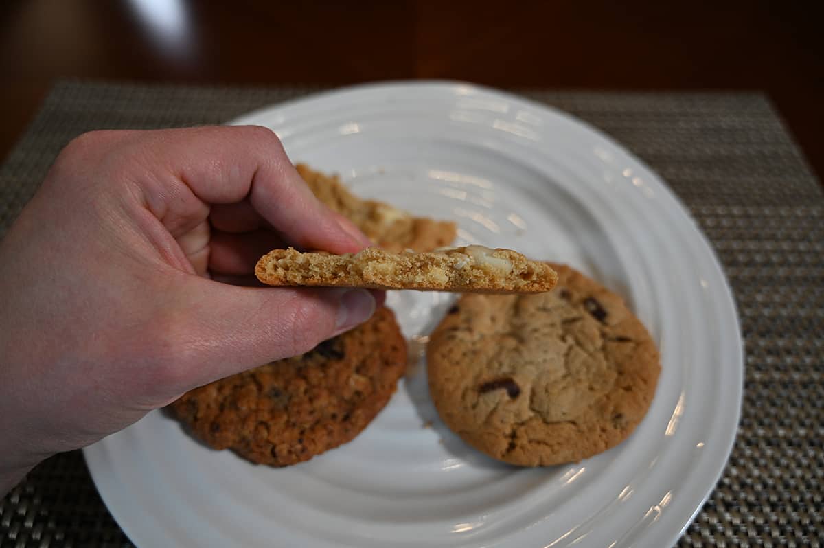 Closeup side view image of a hand holding a double nut cookie with a few bites taken out of it so you can see the center.