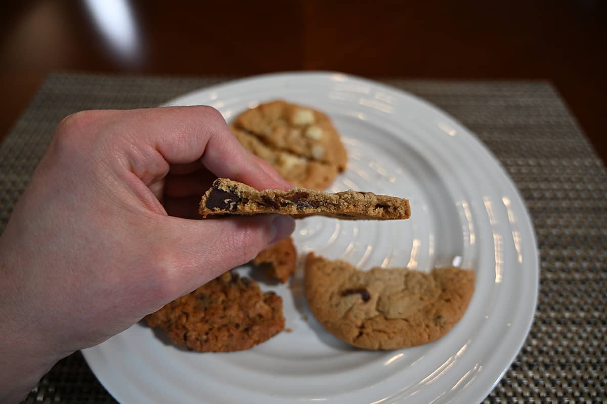 Side view image of a hand holding a chocolate chunk cookies with a few bites taken out of it so you can see the center of the cookie.