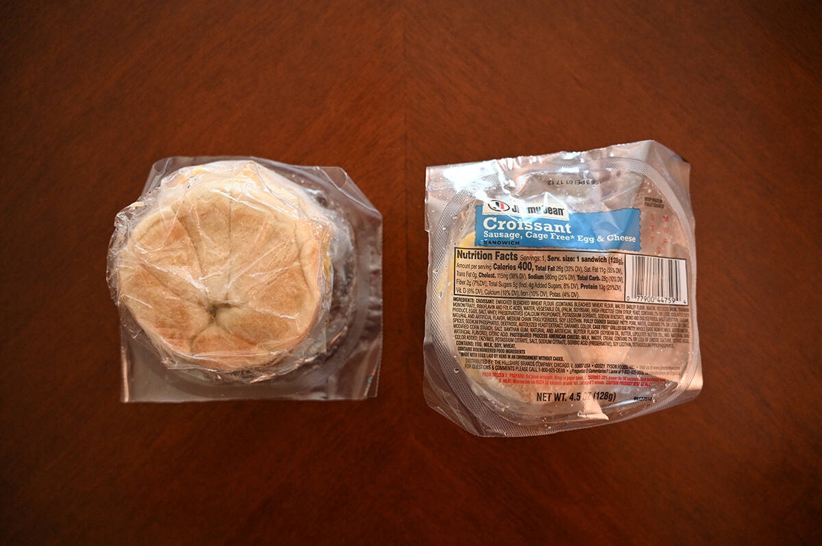 Image of two croissant sandwiches individually wrapped in plastic packaging sitting on a table. 