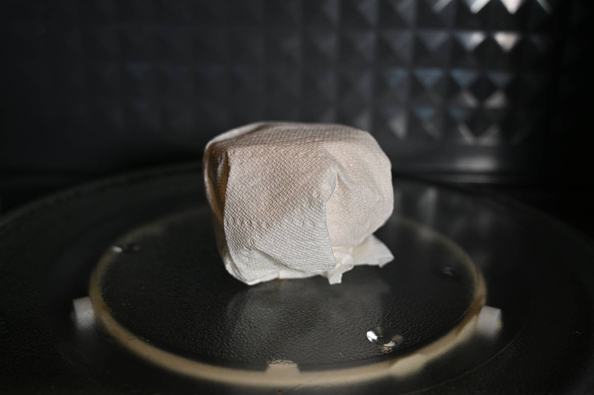 Image of a croissant sandwich wrapped in paper towel and sitting in a microwave ready to be heated.
