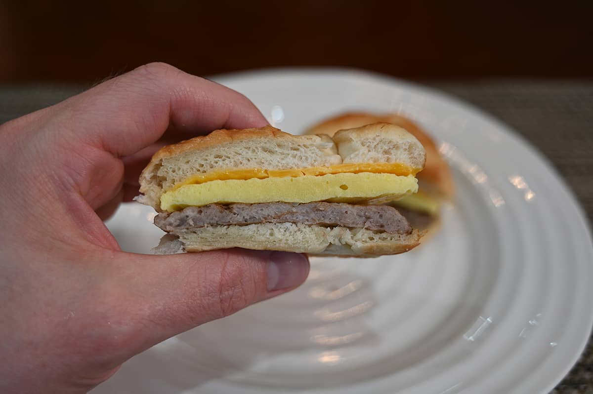 Closeup image of a hand holding a croissant sandwich that's been cut in half so you can see the egg, sausage and cheese in the middle.