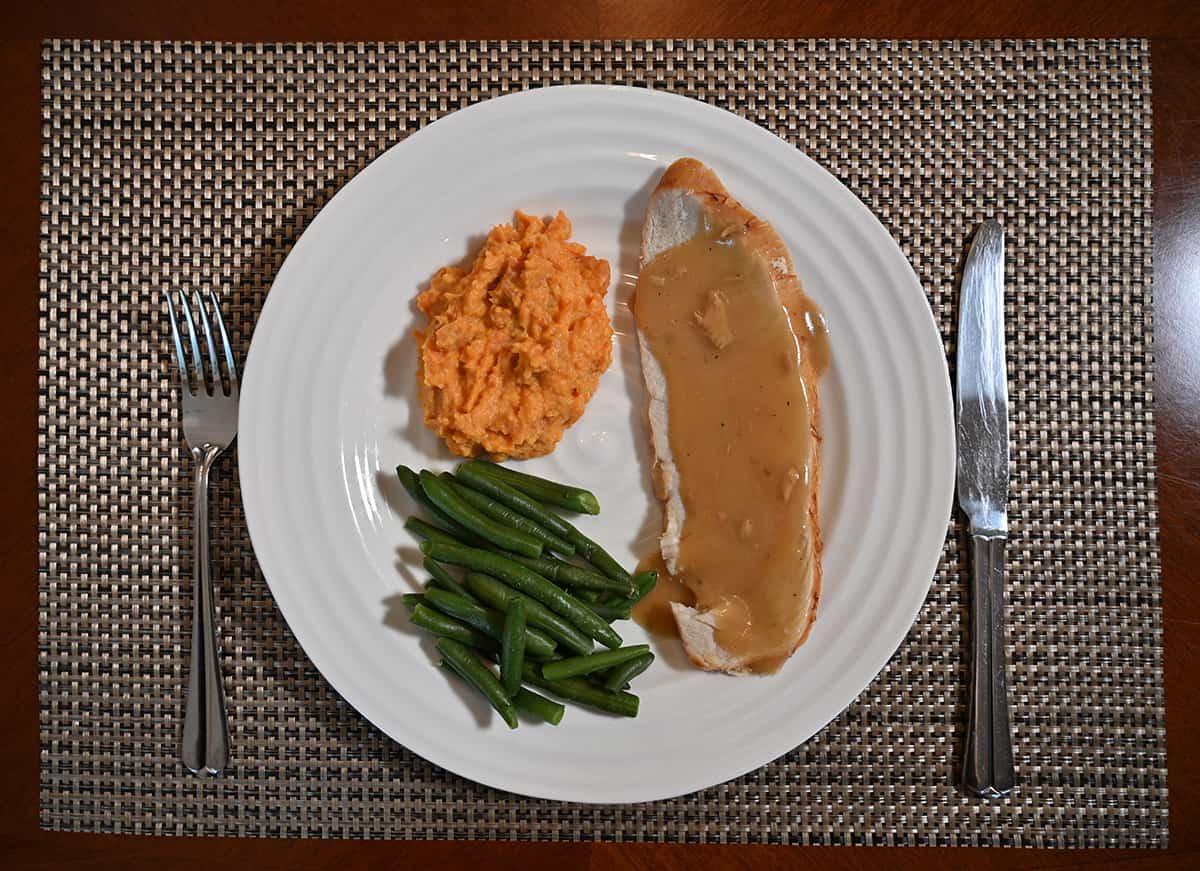 Top down image of a white dinner plate with turkey and gravy, mashed sweet potatoes and green beans served on the plate.