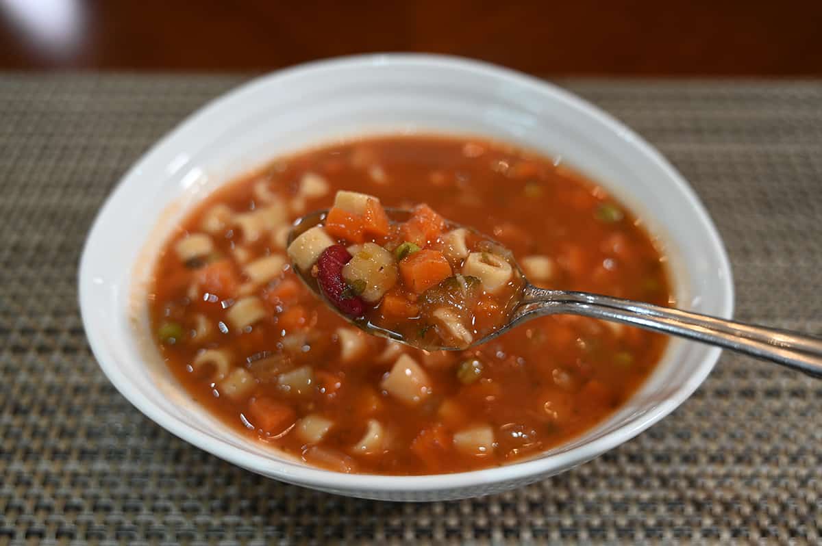 Side view close up image of a bowl of minestrone soup with a spoonful of soup hovering over the bowl.