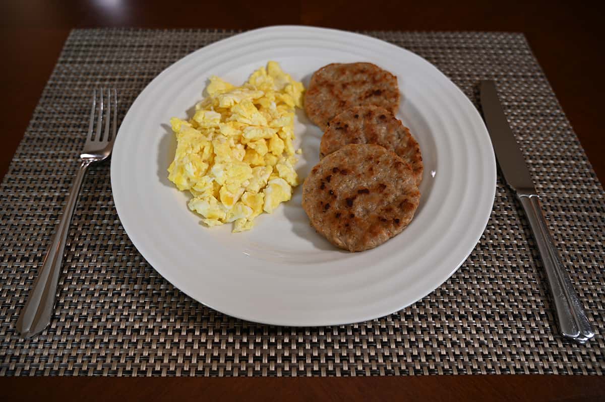 Top down image of a white plate with sctambled eggs and three cooked sausage rounds on it.