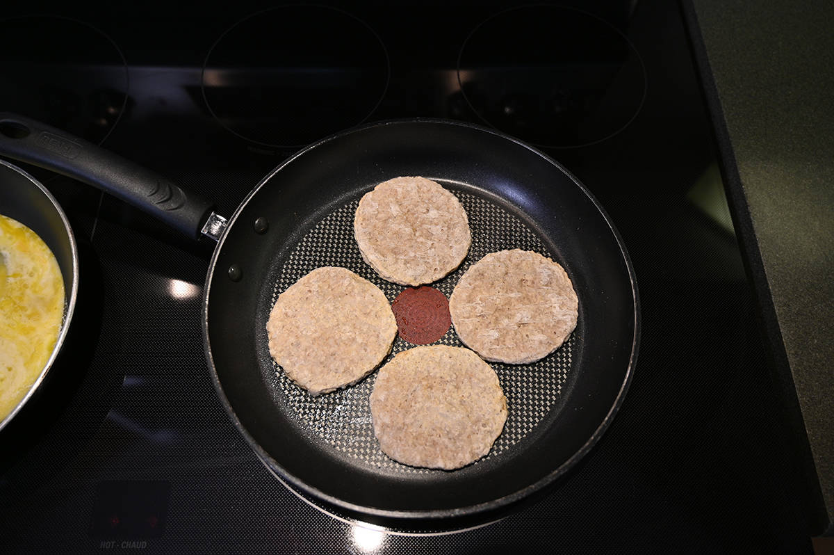 Top down image of a pan with four sausage rounds cooking in it on the top of a stove.