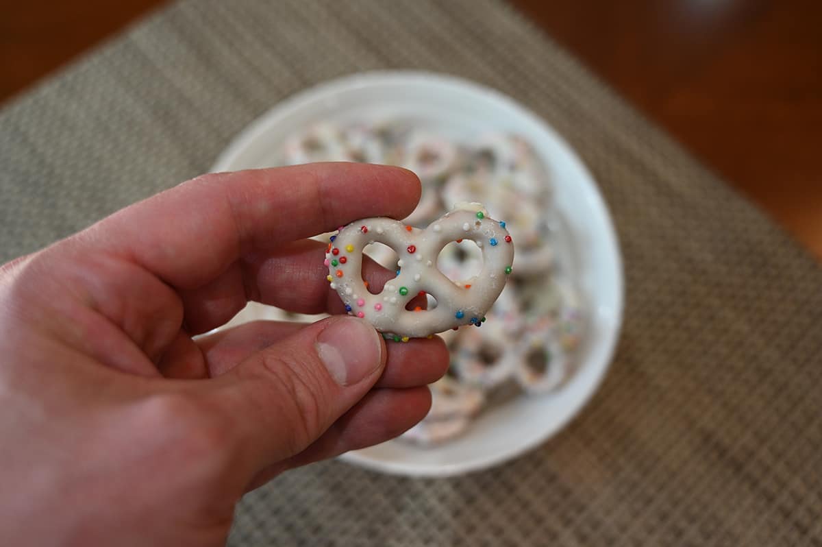 Closeup image of a hand holding one birthday cake yogurt pretzel over a bowl of birthday cake yogurt pretzels.