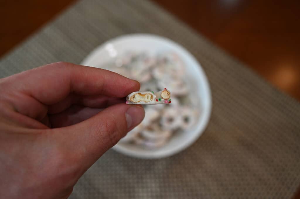 Closeup imasge of a hand holding one birthday cake yogurt pretzel with a bite taken out of it so you can see the inside of the pretzel.