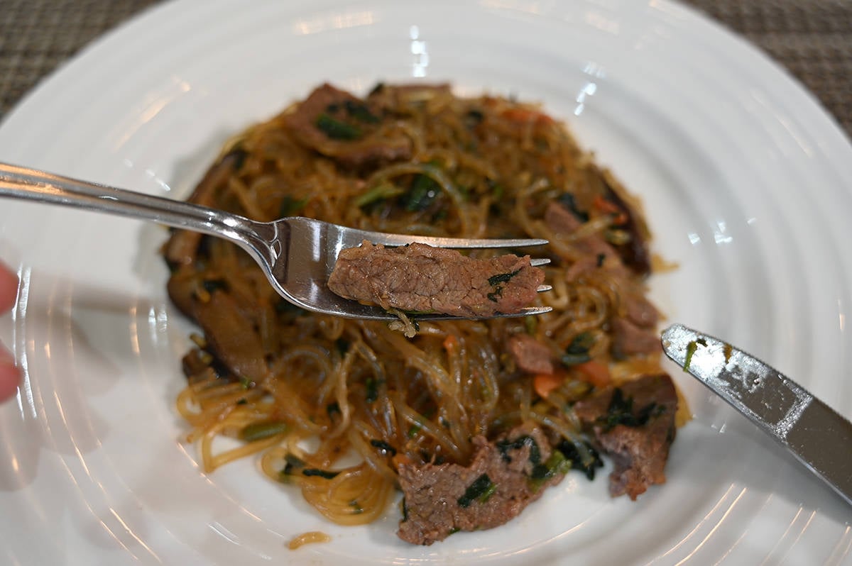 Closeup image of one piece of beef from the japchae on a fork infront of the camera so you can see it closely.