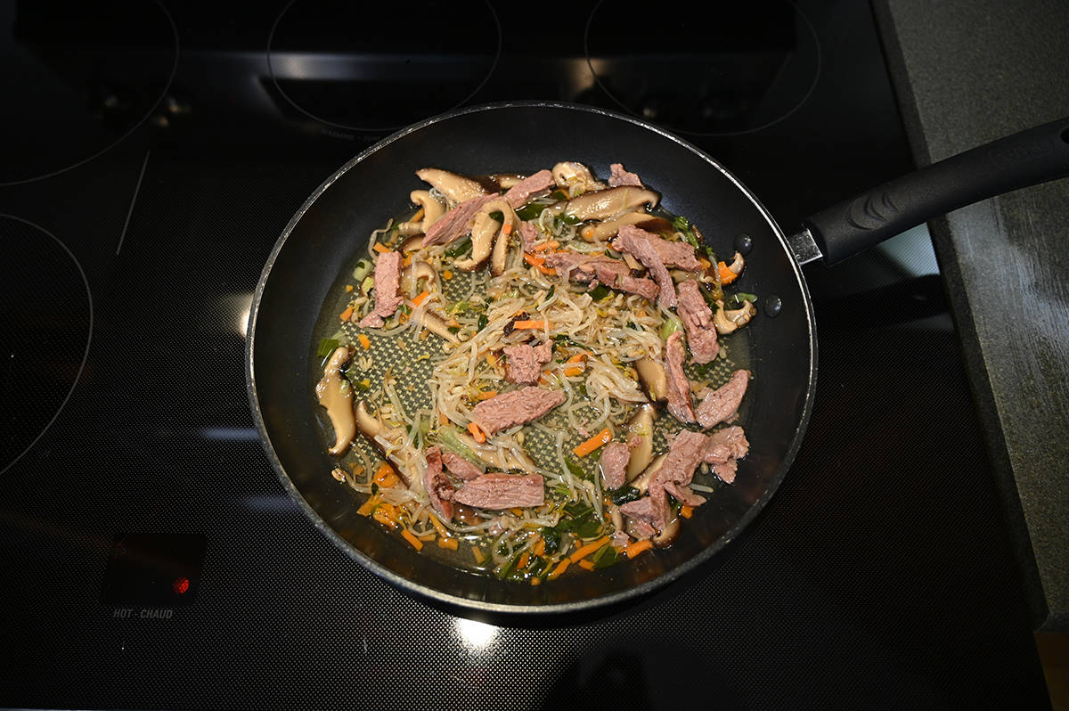 Top down image of the beef and vegetables from the package cooking in  a frying pan on the stove.