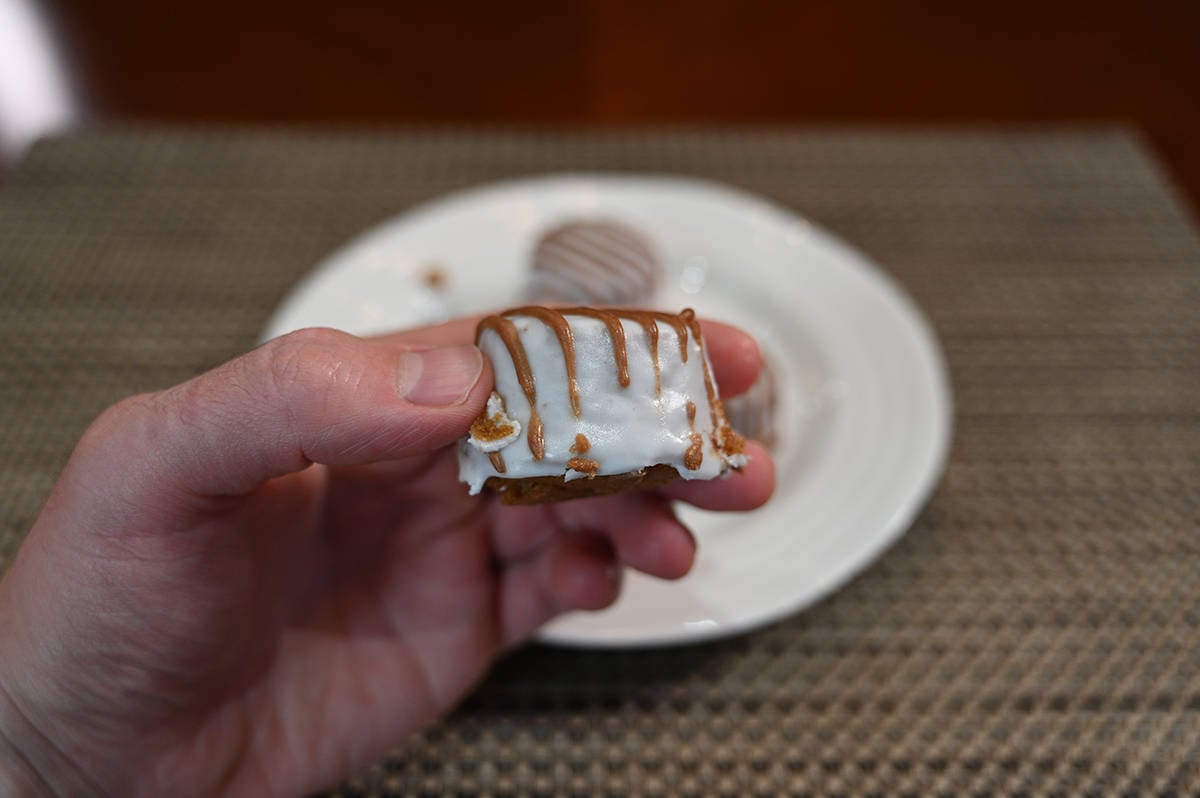 Closeup side view image of a hand holding one pumpkin spice bite close to the camera, you can see a thick layer of icing on it.