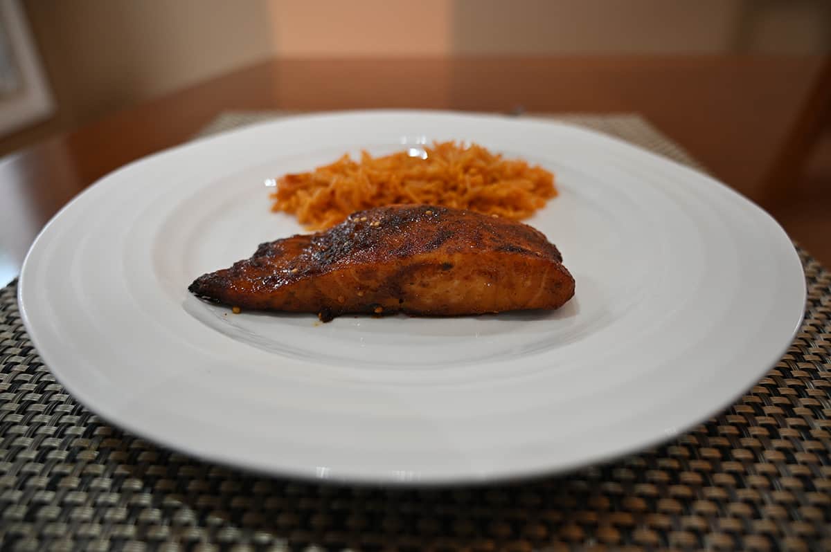 Side view image of a baked fillet on a white plate served beside some rice.