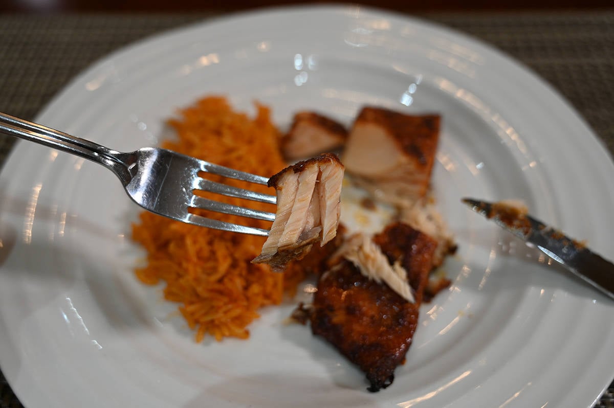 Closeup image of a forkful of salmon showing how flaky the salmon is. In the background is a plate of rice and salmon.