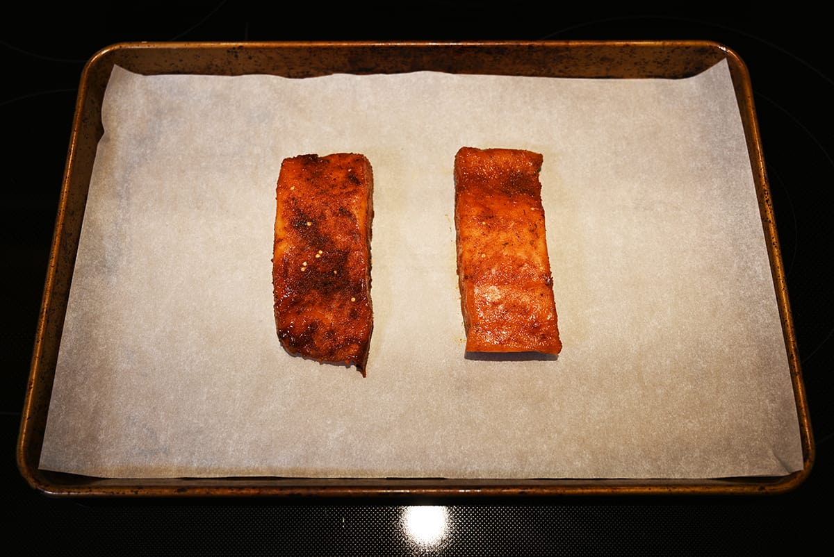 Top down image of two salmon fillets on a parchment lined baking sheet after being baked.