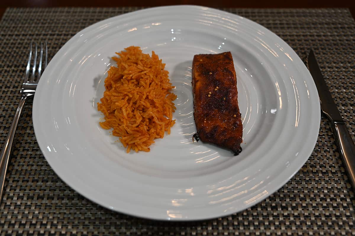  Top down side view image of a baked salmon fillet beside a pile or rice, served on a white plate.
