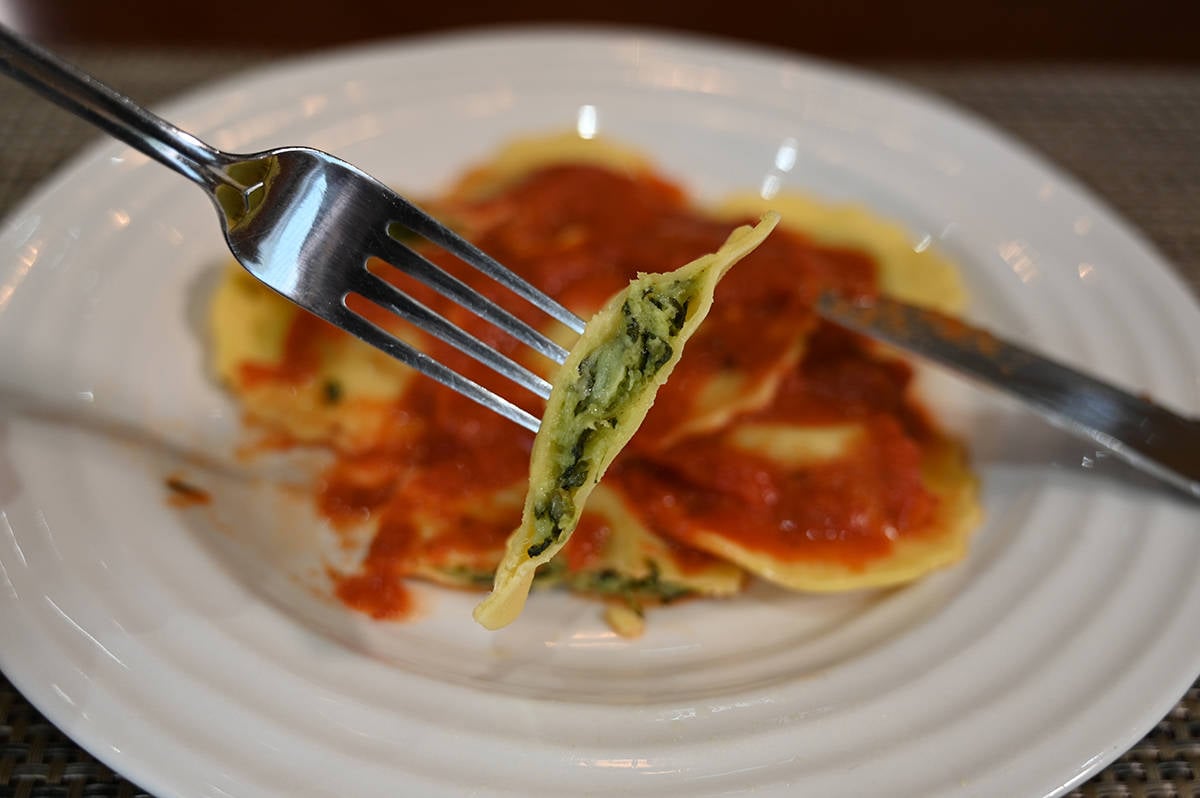 Closeup of one ravioli on a fork that's had a bite taken out of it so you can see the spinach and cheese filling.