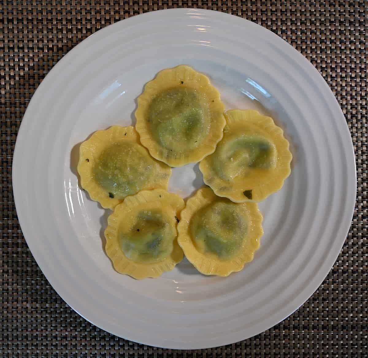 Top down image of a white plate with five ravioli served on it, the ravioli do not have any sauce.