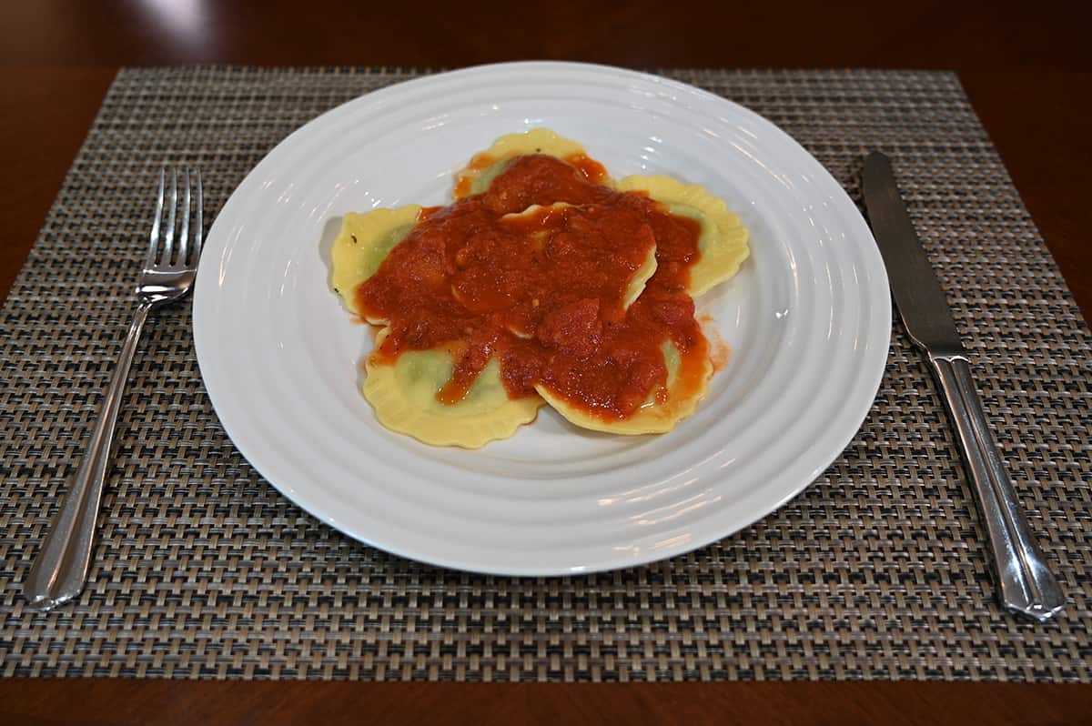 Image of a plate of prepared ravioli with a red sauce on top of it, beside the plate is a fork and knife.