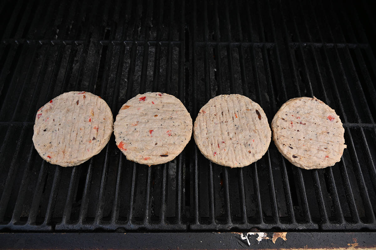 Top down image of four burgers being cooked on a barbecue.