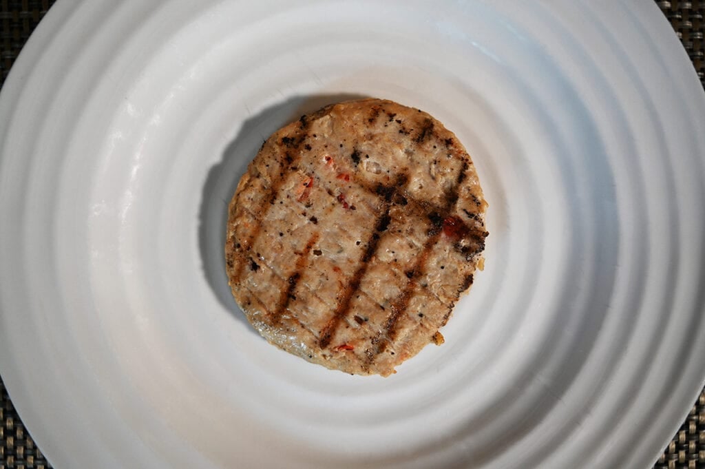 Top down image of a cooked chicken patty served on a white plate, the patty has grill marks on it.
