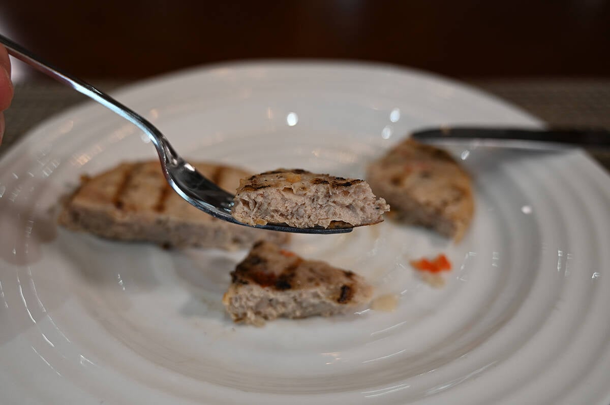 Closeup image of a fork with a piece of chicken burger patty on it so you can see the center of the patty. The rest of the burger is in the background of the photo.