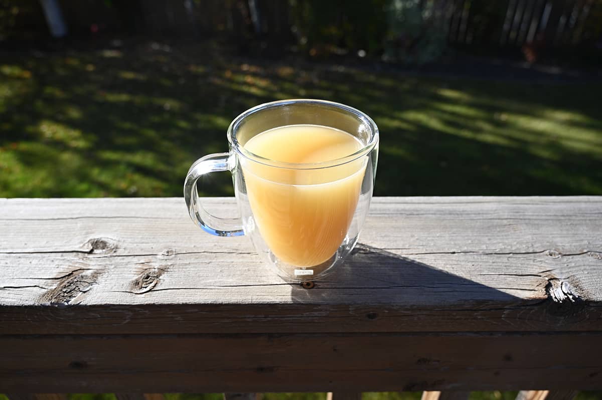 Top down image of a mug of bone broth sitting on a deck with trees in the background. The broth has been partially drank.