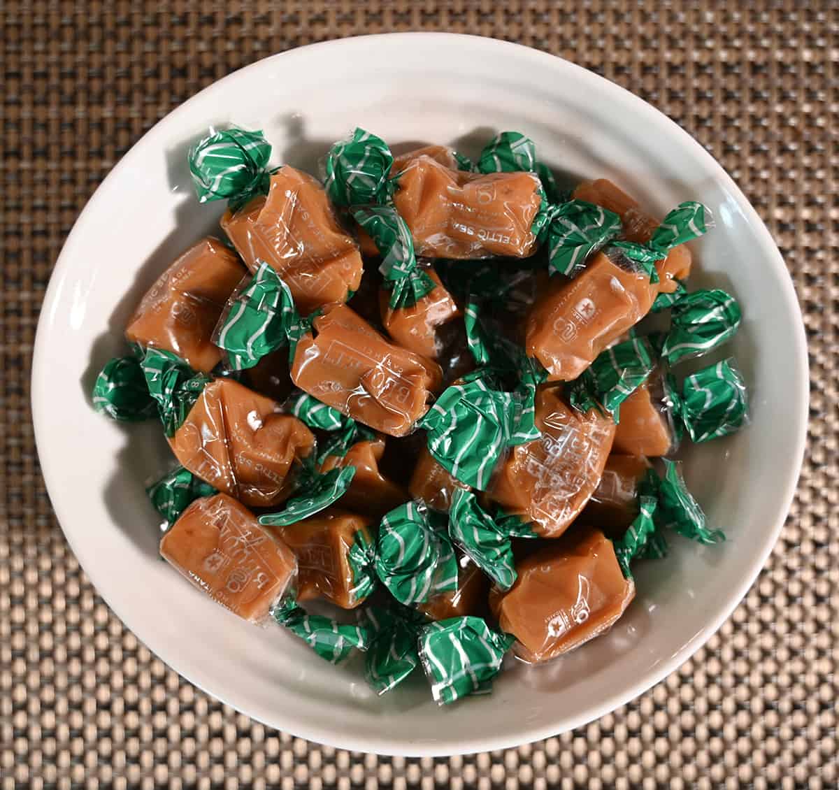 Top down image of a bowl of caramel candies wrapped in clear plastic.