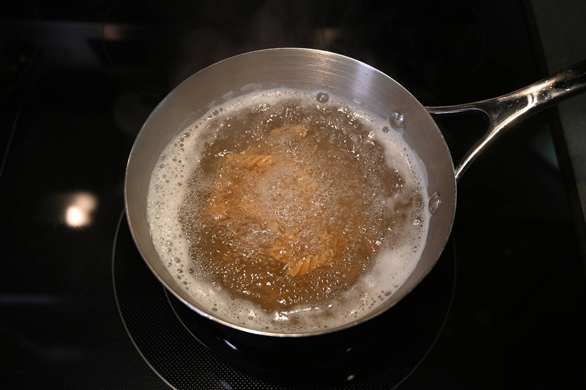Top down image of a pot of boiling water on a stovetop with pasta in it cooking.