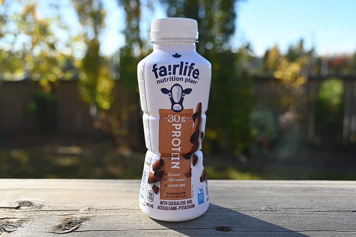 Image of one bottle of Costco Chocolate Fairlife Protein Shake sitting on a deck outside with trees in the background.