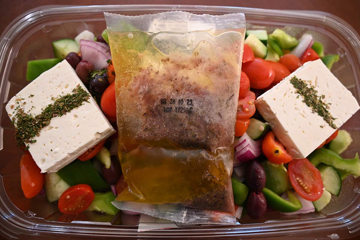 Top down closeup image of the packet of vinaigrette sitting on top of the opened Greek salad.