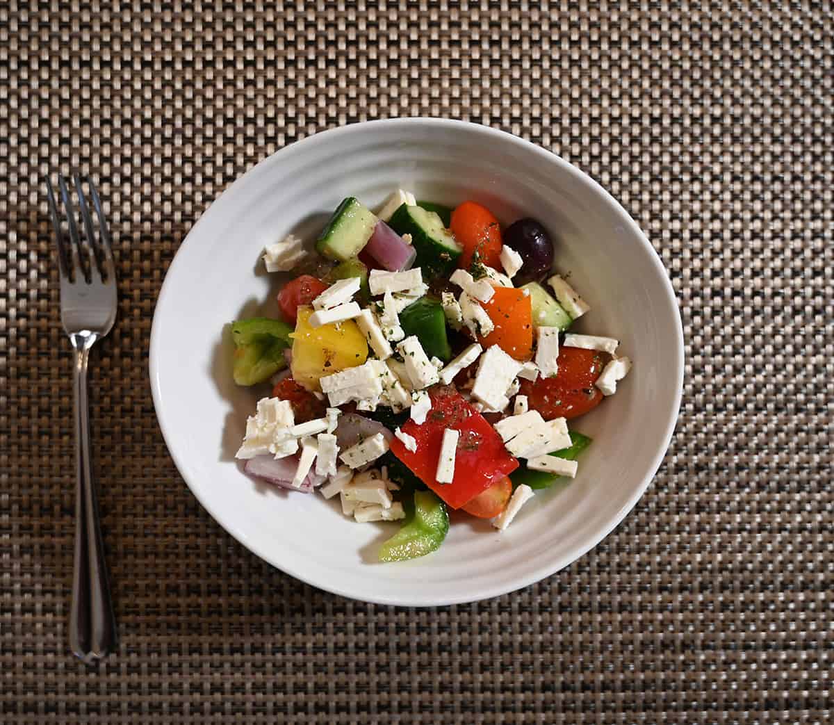 Top down image of the greek salad served in a white bowl with crumbled feta on top.