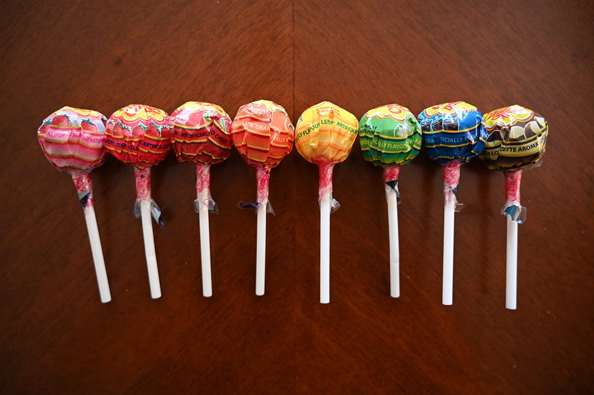 Top down image of eight different flavors of Chupa Chup lollipops unopened laying on a table.