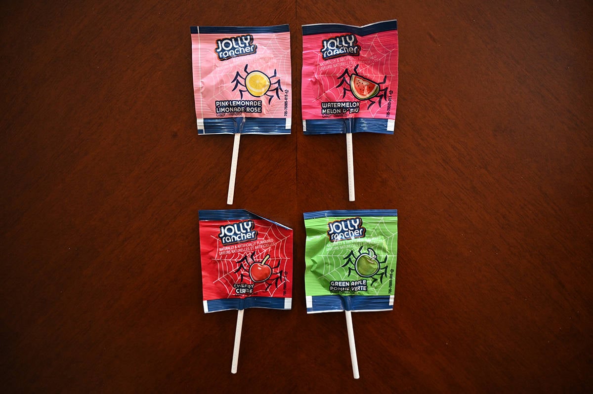 Top down image of four different kinds of Jolly Rancher lollipops on a table, unopened.