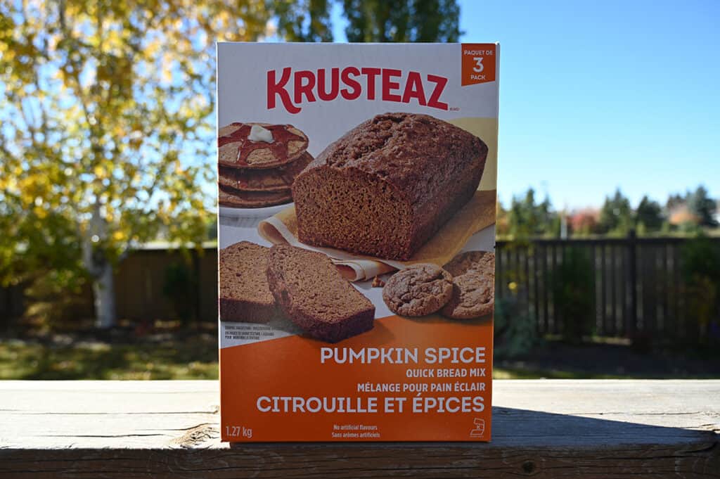 Image of the Costco Krusteaz Pumpkin Spice Quick Bread Mix box sitting on a deck outside with trees in the background.